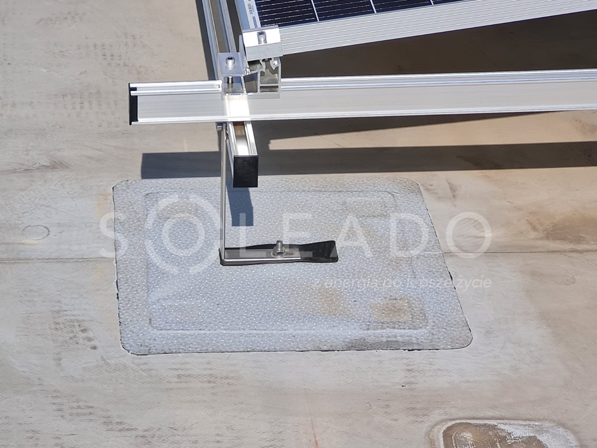 Mocowanie aluminiowej konstrukcji wsporczej paneli słonecznych do dachu, uszczelnione kwadratową podkładką z widocznym znakiem wodnym firmy.