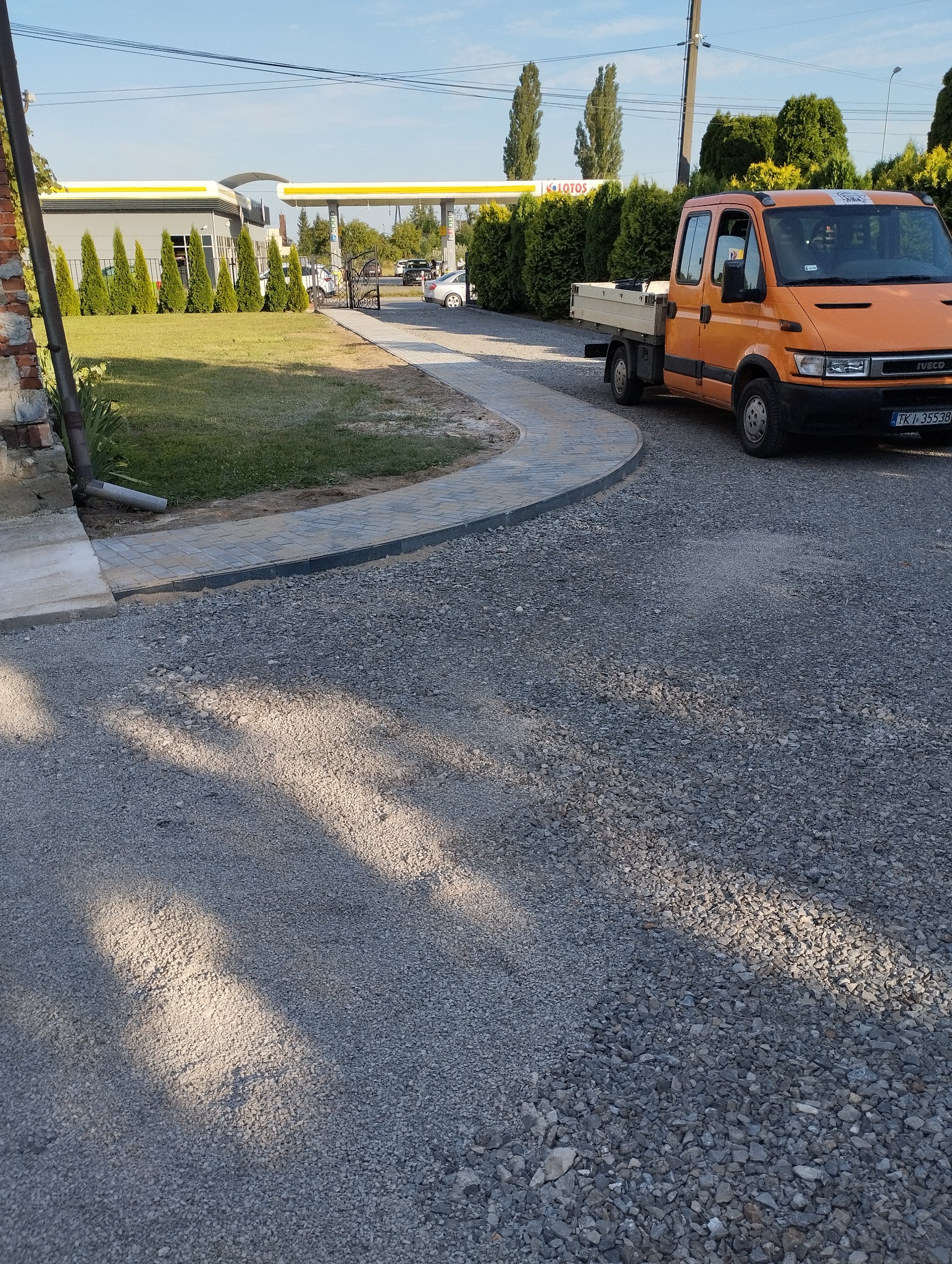 Ułożona ścieżka z kostki brukowej prowadząca do stacji benzynowej, z pomarańczowym samochodem dostawczym zaparkowanym obok.