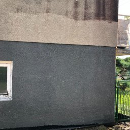 Hugo clean - Fragment elewacji budynku z widocznym podziałem na dwie warstwy tynku: górna, jaśniejsza, z widocznymi zaciekami i zabrudzeniami, oraz dolna, ciemnoszara, świeżo nałożona. Przy elewacji widoczna...