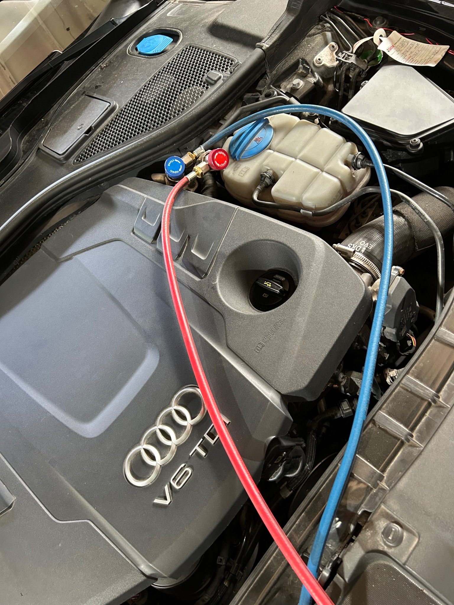 Silnik Audi V6 TDI z podłączonymi przewodami serwisowymi klimatyzacji, widoczne złącza z manometrami w kolorach czerwonym i niebieskim.