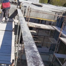 Łukasz Wleczyk - Wznoszenie konstrukcji betonowej z użyciem szalunków i rusztowań, widok z góry na plac budowy w słoneczny dzień.