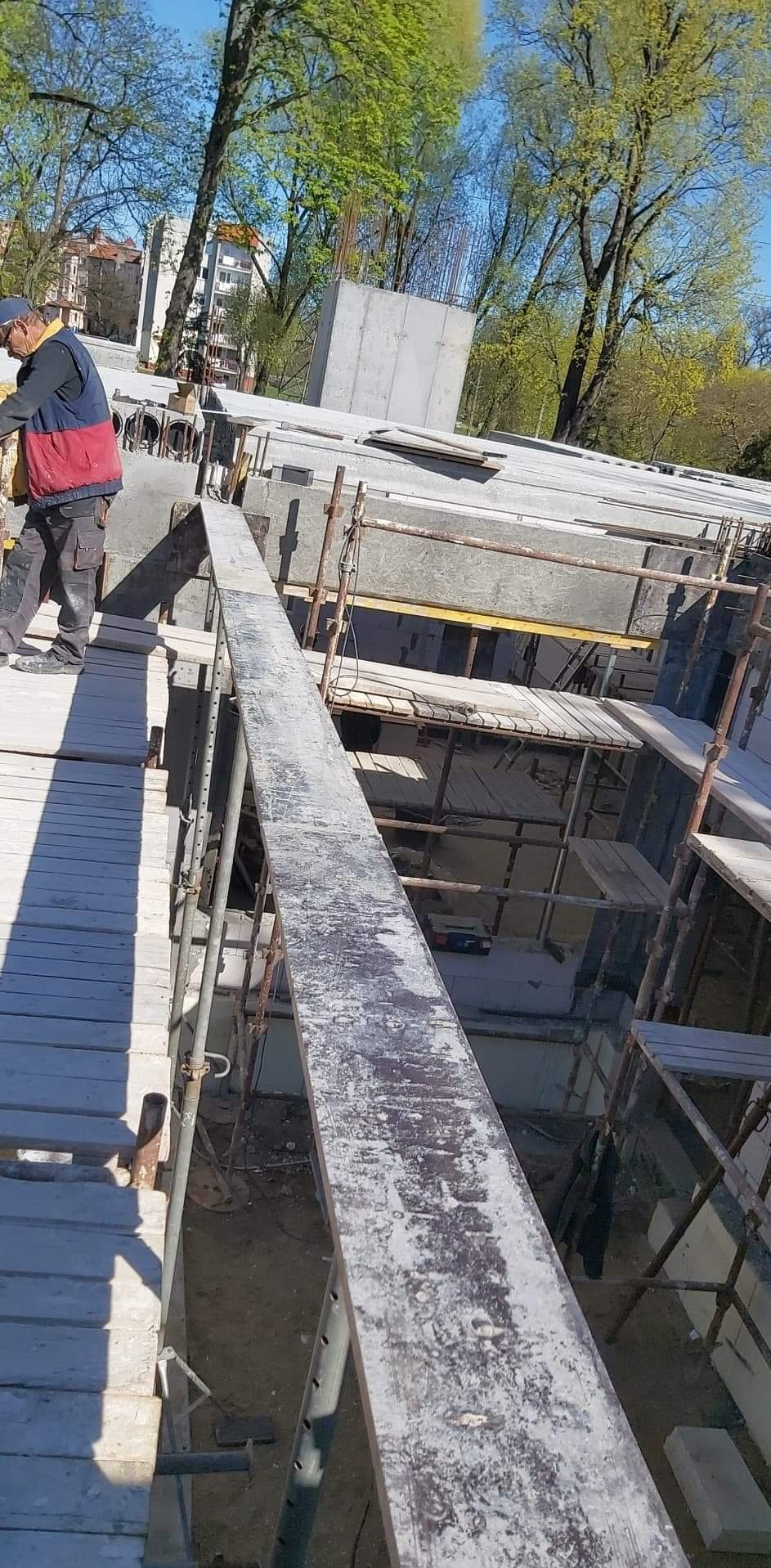 Wznoszenie konstrukcji betonowej z użyciem szalunków i rusztowań, widok z góry na plac budowy w słoneczny dzień.