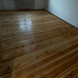 Świeżo wycyklinowana, lakierowana podłoga z desek w pustym pokoju z grzejnikiem pod oknem.