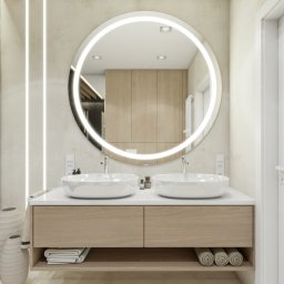 AG Design & Estate - Nowoczesna łazienka z dwoma umywalkami nablatowymi, okrągłym lustrem z podświetleniem LED, drewnianą szafką podumywalkową i dekoracyjnymi wazonami ceramicznymi obok szklanej kabiny prysznicowej.