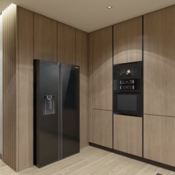 AG Design & Estate - Nowoczesna kuchnia z drewnianymi frontami szafek, czarnym sprzętem AGD (lodówka side-by-side i piekarnik wielofunkcyjny) oraz roślinami w szklanych wazonach na parapecie okiennym.