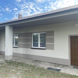 Michał Szymczuk - Odnowiona elewacja budynku świetlicy wiejskiej z pomalowanymi pasami w odcieniach szarości i beżu, brązowe drzwi wejściowe i okna z firankami, widok na jasne, lekko zachmurzone niebo.