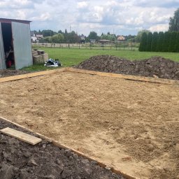 Michał Szymczuk - Przygotowany teren pod wylewkę fundamentów z drewnianym szalunkiem, widoczna sterta ziemi i blaszany garaż w tle.