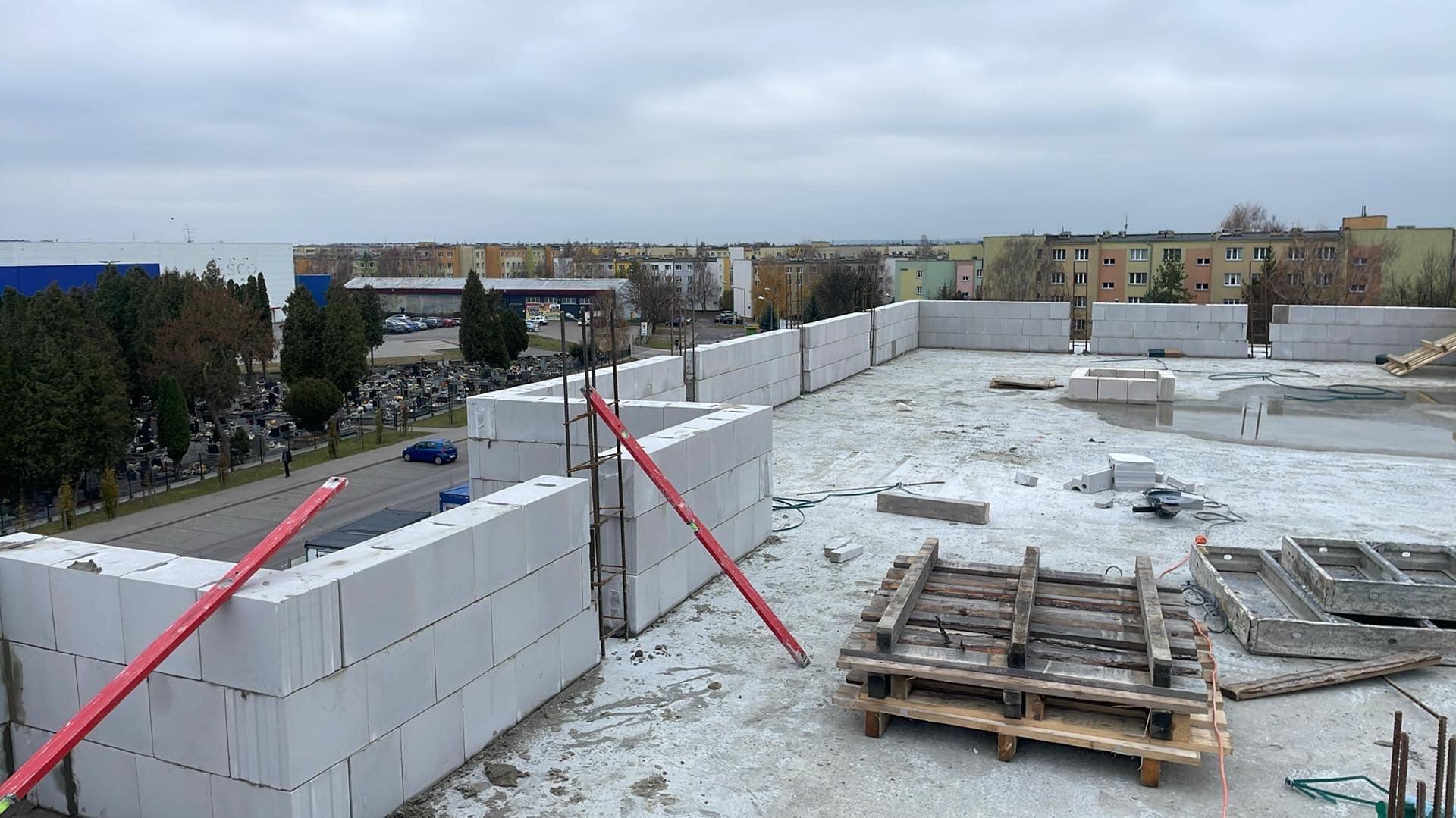 Wznoszenie ścian attyki z bloczków na dachu budynku w Hrubieszowie, widoczne poziomice i elementy konstrukcyjne.