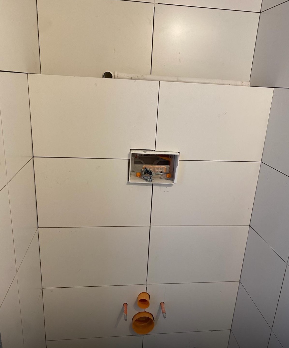 Białe płytki ścienne w łazience z widoczną instalacją podtynkową i rurami odpływowymi. Etap prac wykończeniowych, widok z dołu.