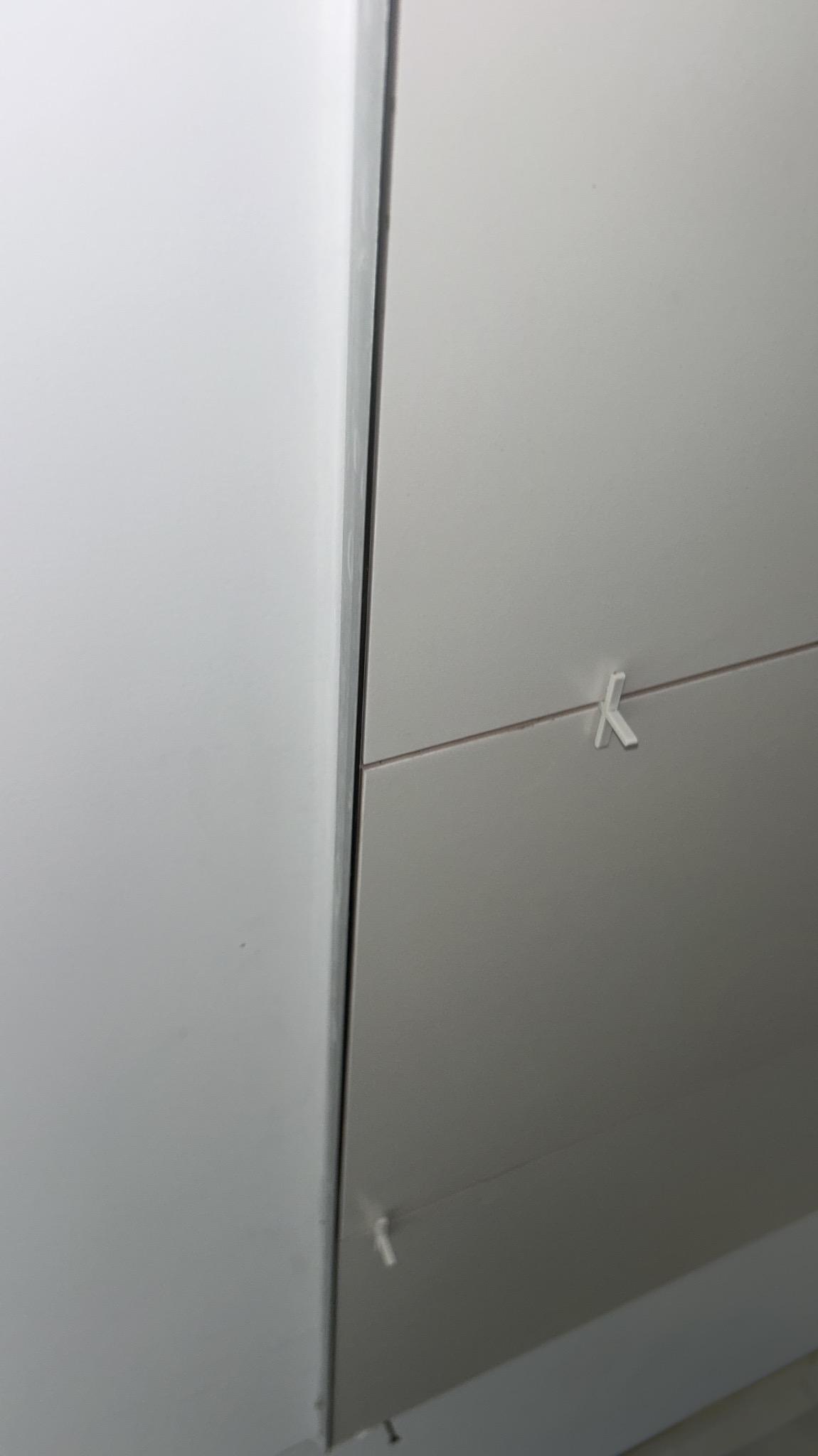 Świeżo ułożone, jasne płytki ścienne z krzyżykami dystansowymi, widoczne fugi. Minimalistyczne wykończenie łazienki w nowoczesnym stylu.