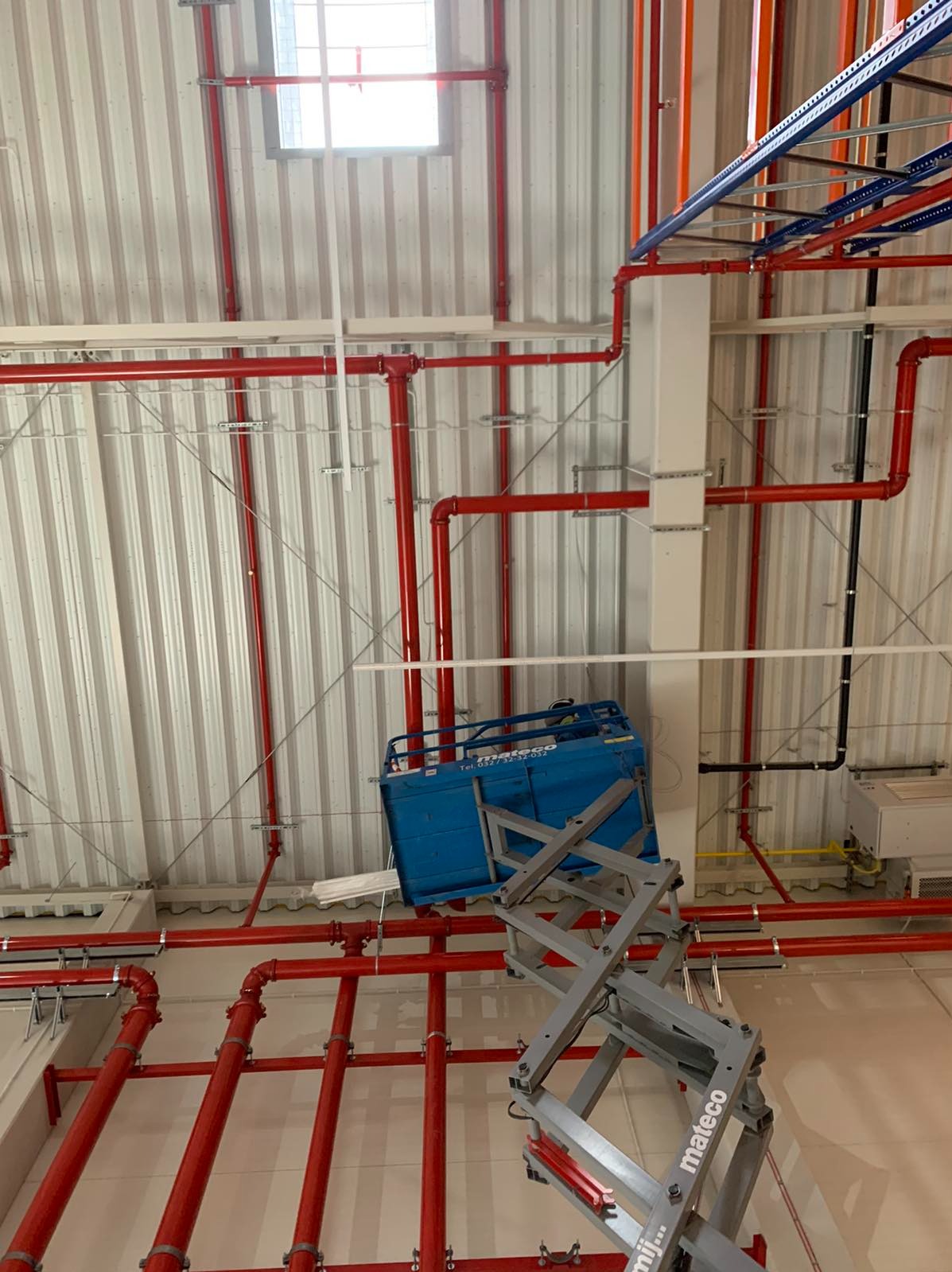 Wnętrze hali z widoczną instalacją przeciwpożarową w kolorze czerwonym, montowaną z użyciem podnośnika koszowego marki Mateco.