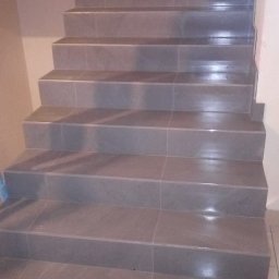 Bau Consult Vitalii Sliusarenko - Wykończone schody z szarymi płytkami, widok z dołu. Czyste fugi, równe krawędzie. Detal wykończenia wnętrza z bliska.