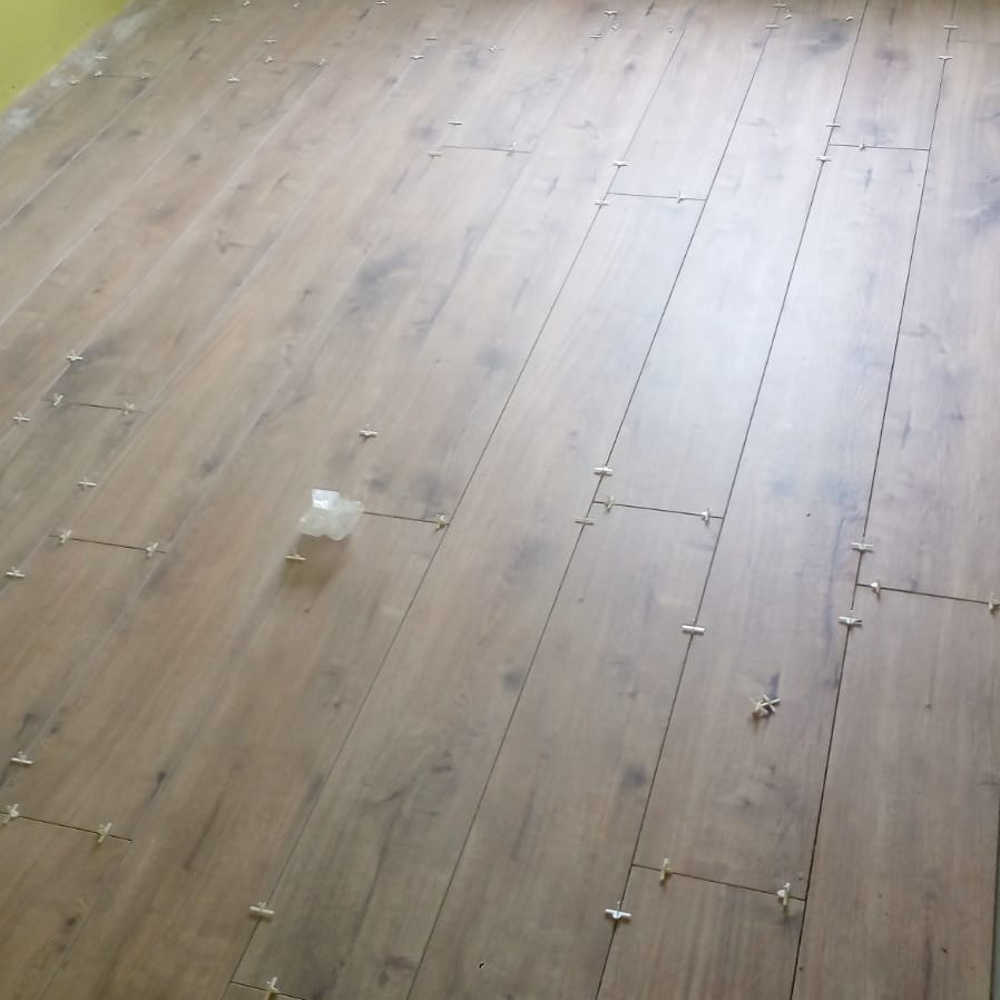 Układanie paneli podłogowych z użyciem krzyżyków dystansowych, widok z góry na fragment podłogi w trakcie montażu. Jasne panele z imitacją drewna.