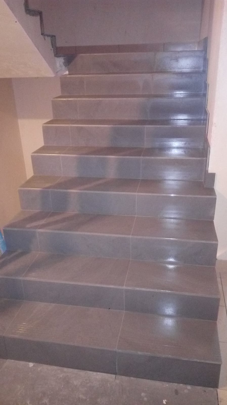 Wykończone schody z szarymi płytkami, widok z dołu. Czyste fugi, równe krawędzie. Detal wykończenia wnętrza z bliska.