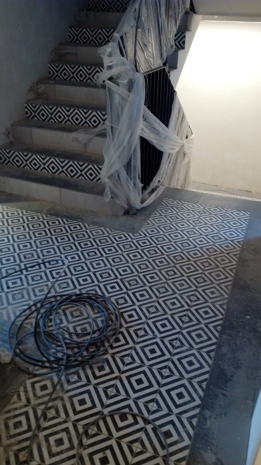 Ukończona podłoga i schody z wzorem geometrycznym, zabezpieczone elementy, kabel na podłodze, wykończenie wnętrz w trakcie realizacji.