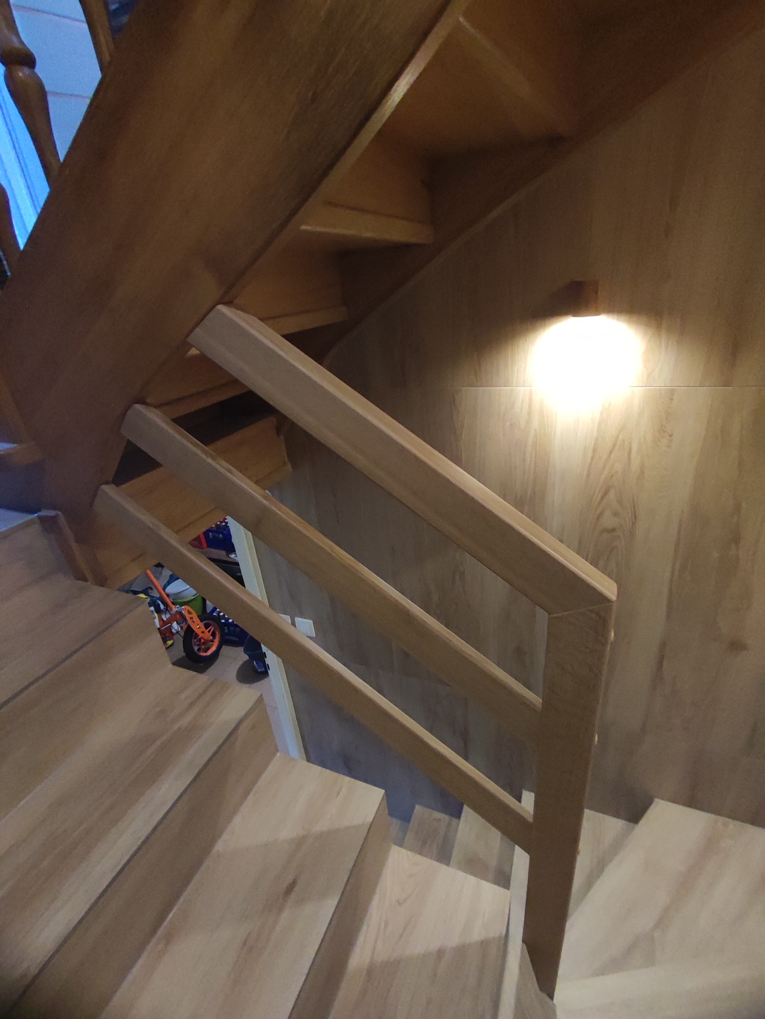 Drewniane schody z jasnymi panelami, proste balustrady i widoczne zabawki dziecięce w tle.