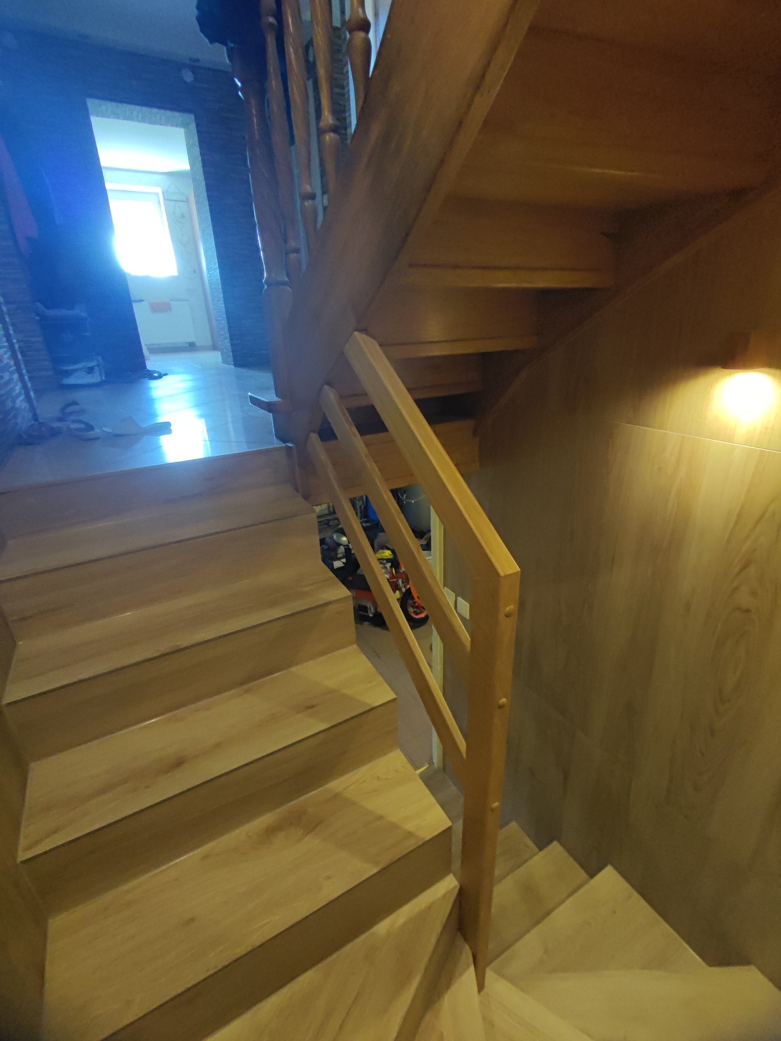 Drewniane schody z jasnego drewna z balustradą, widok z dołu, jasne światło w tle.