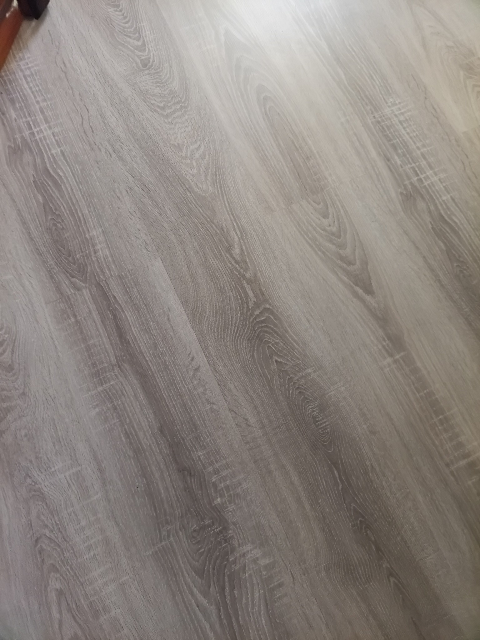 Świeżo ułożone panele podłogowe w odcieniach szarości z widoczną strukturą drewna, ułożone pod kątem, z delikatnym połyskiem.