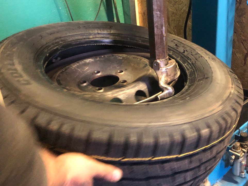 Demontaż opony z felgi przy użyciu specjalistycznej maszyny w warsztacie wulkanizacyjnym, widoczne narzędzie do zdejmowania opon i fragment dłoni.