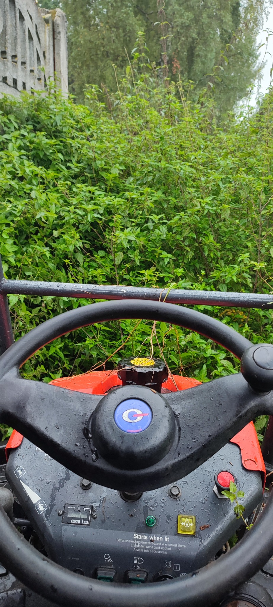 Widok z perspektywy operatora na zarośnięty teren zza kierownicy traktora w Czerwieńsku. Zarośla sięgają wysokości ogrodzenia.