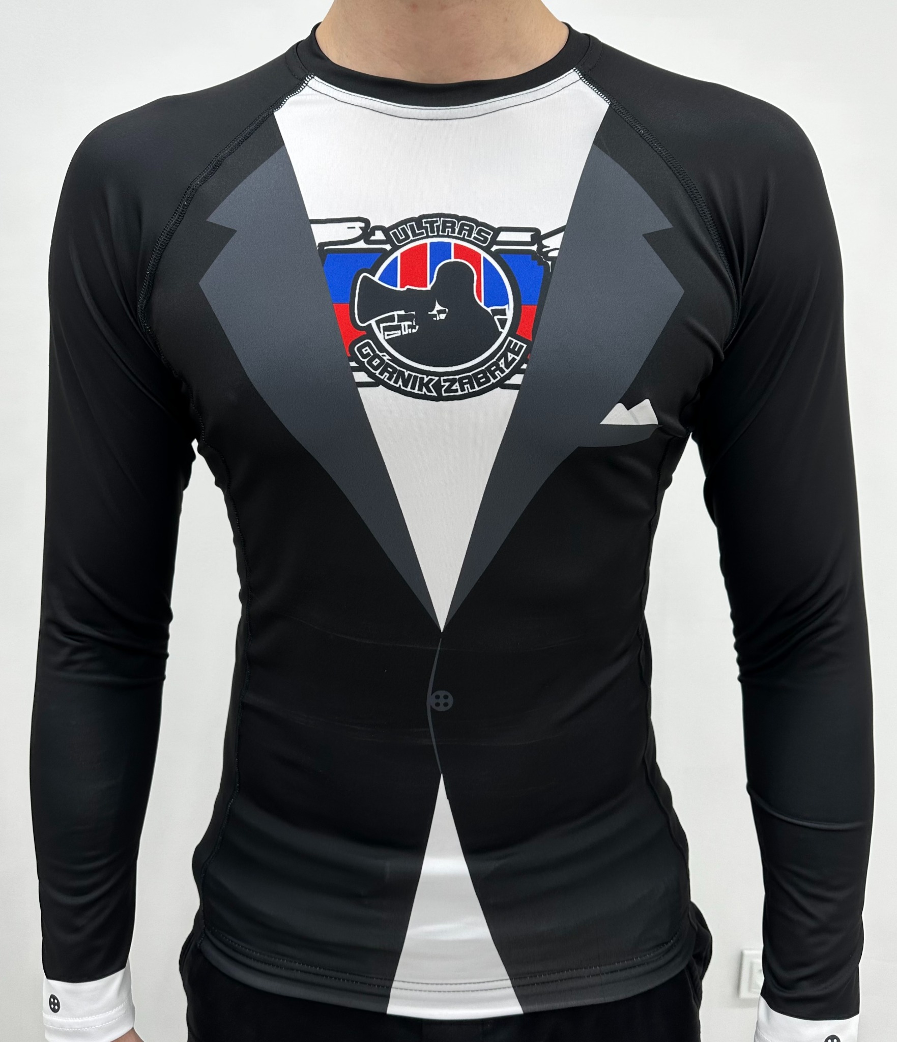 Męska koszulka sportowa z długim rękawem, imitująca smoking z nadrukiem logo kibiców Górnika Zabrze, na białym tle.