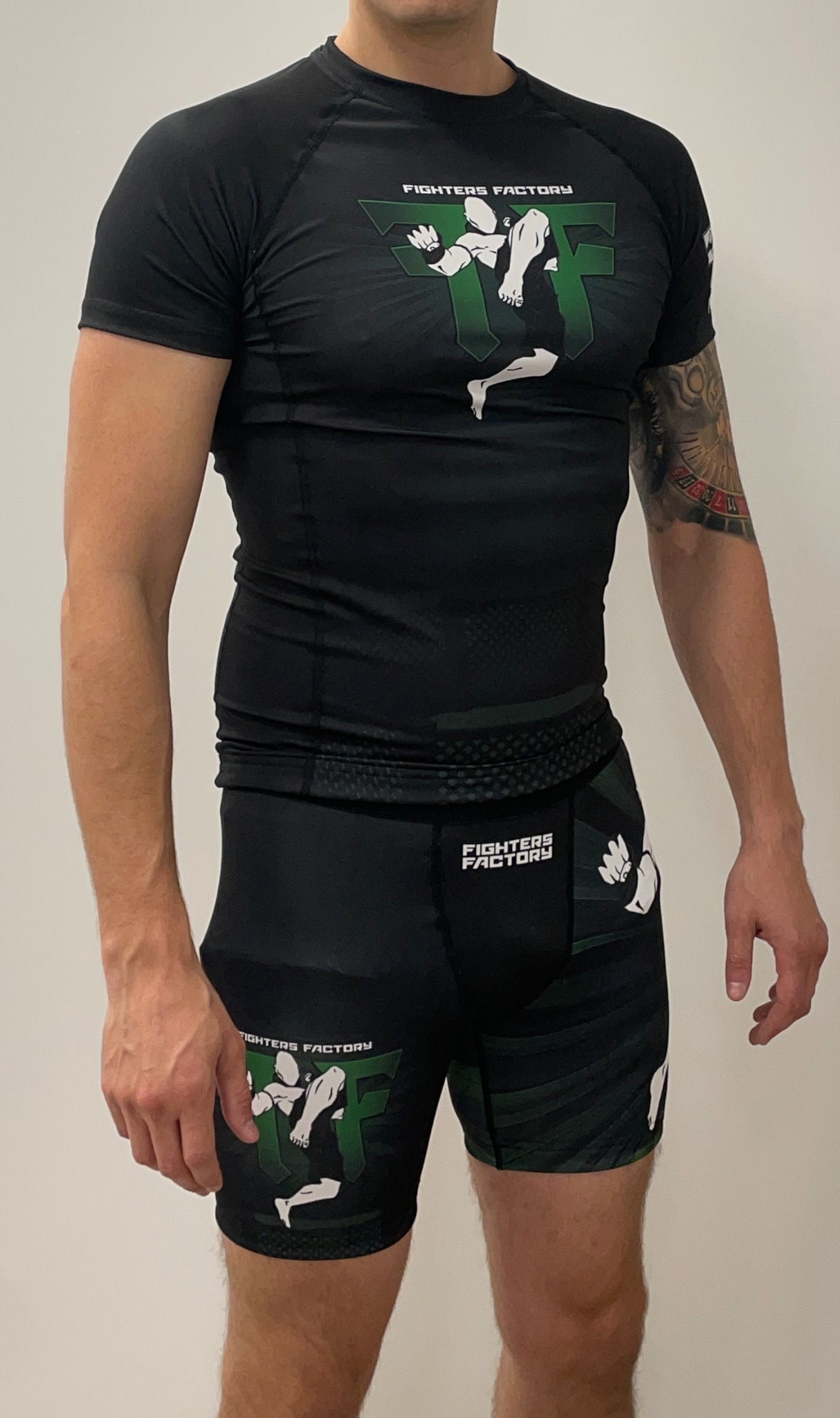 Mężczyzna w czarnym komplecie odzieży sportowej z nadrukiem logo Fighters Factory, prezentujący strój na białym tle.