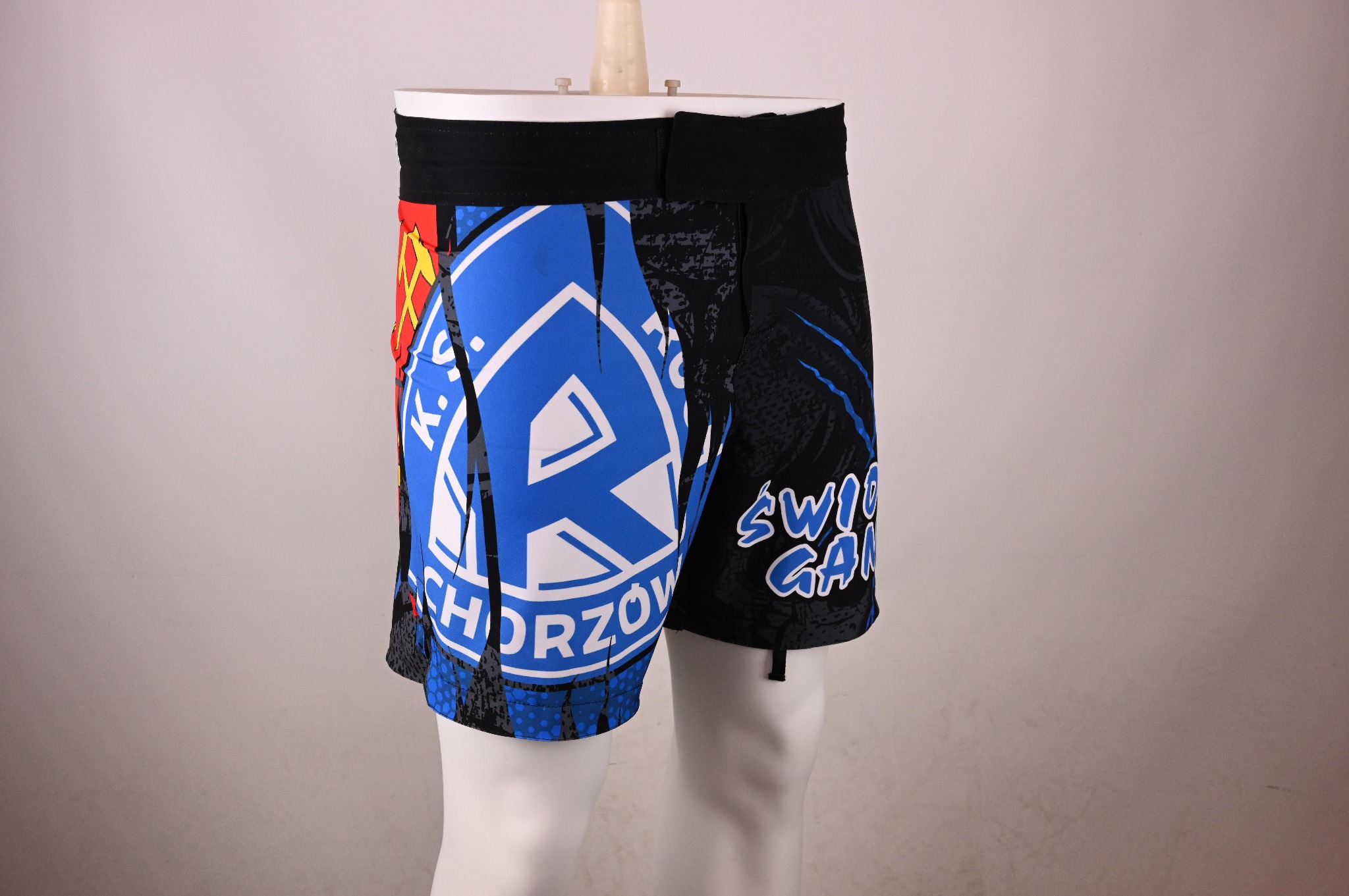 Szorty sportowe z nadrukiem klubowym, widoczne logo i nazwa klubu 'Ruch Chorzów' oraz grafika w kolorach niebieskim, białym, czerwonym i żółtym, prezentowane na manekinie na neutralnym tle.
