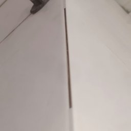 RADOSŁAW ŻARSKI REMONTEXPERT - Białe płytki ścienne z systemem poziomowania, widok z bliska na narożnik. Cienka fuga. Czerwony klin i czarna baza systemu poziomowania płytek.