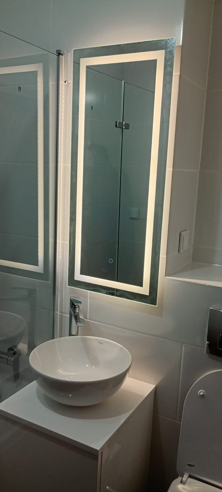 Nowoczesna łazienka: biała umywalka nablatowa, lustro z podświetleniem LED, kabina prysznicowa z szarymi płytkami. Minimalistyczny design i funkcjonalność.