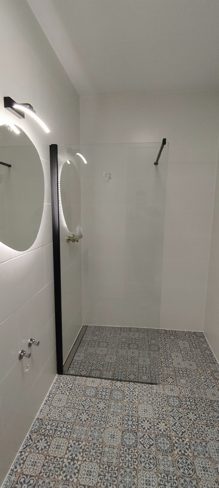 Nowoczesna kabina prysznicowa ze szklaną ścianką i odpływem liniowym, okrągłe lustro z podświetleniem LED, płytki podłogowe w stylu vintage.