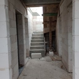 Magdalena Szczepańska BUDIMAG - Wnętrze budynku w trakcie budowy schodów, widoczne białe bloczki konstrukcyjne i drewniane szalunki.