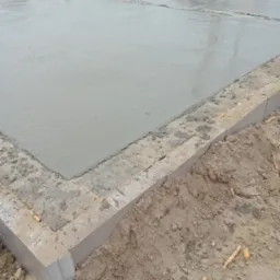 Wylany fundament betonowy w Lublinie, widoczne szalunki i świeży beton. W tle ekipa budowlana i betoniarka.