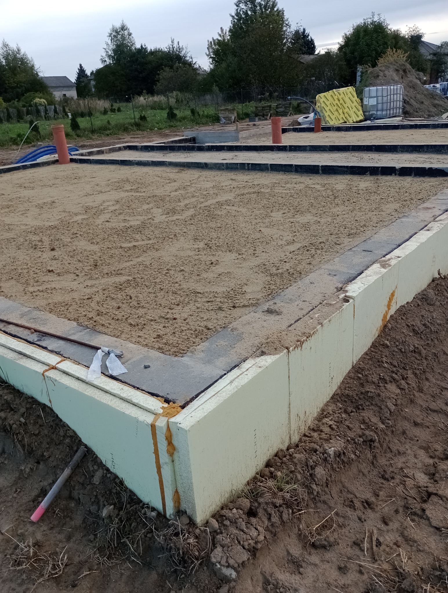 Fundamenty domu jednorodzinnego, ocieplone styropianem, zasypane piaskiem, widoczne rury instalacyjne.