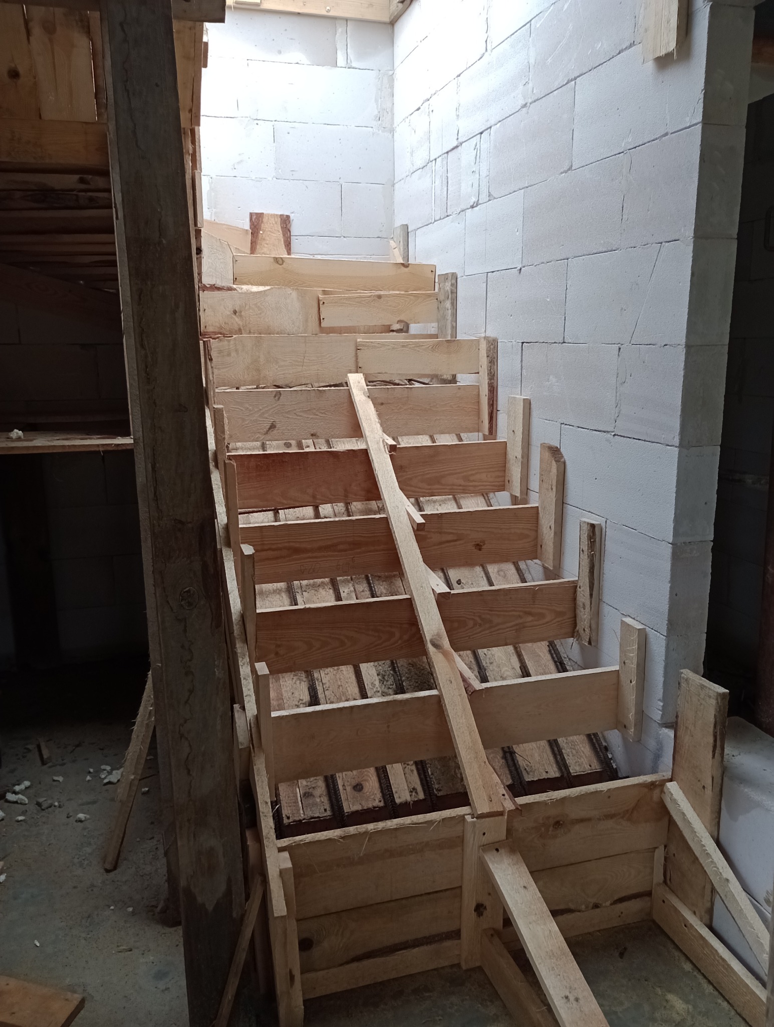 Konstrukcja drewniana szalunku schodów w surowym stanie, widoczne zbrojenie, ściany z betonu komórkowego.