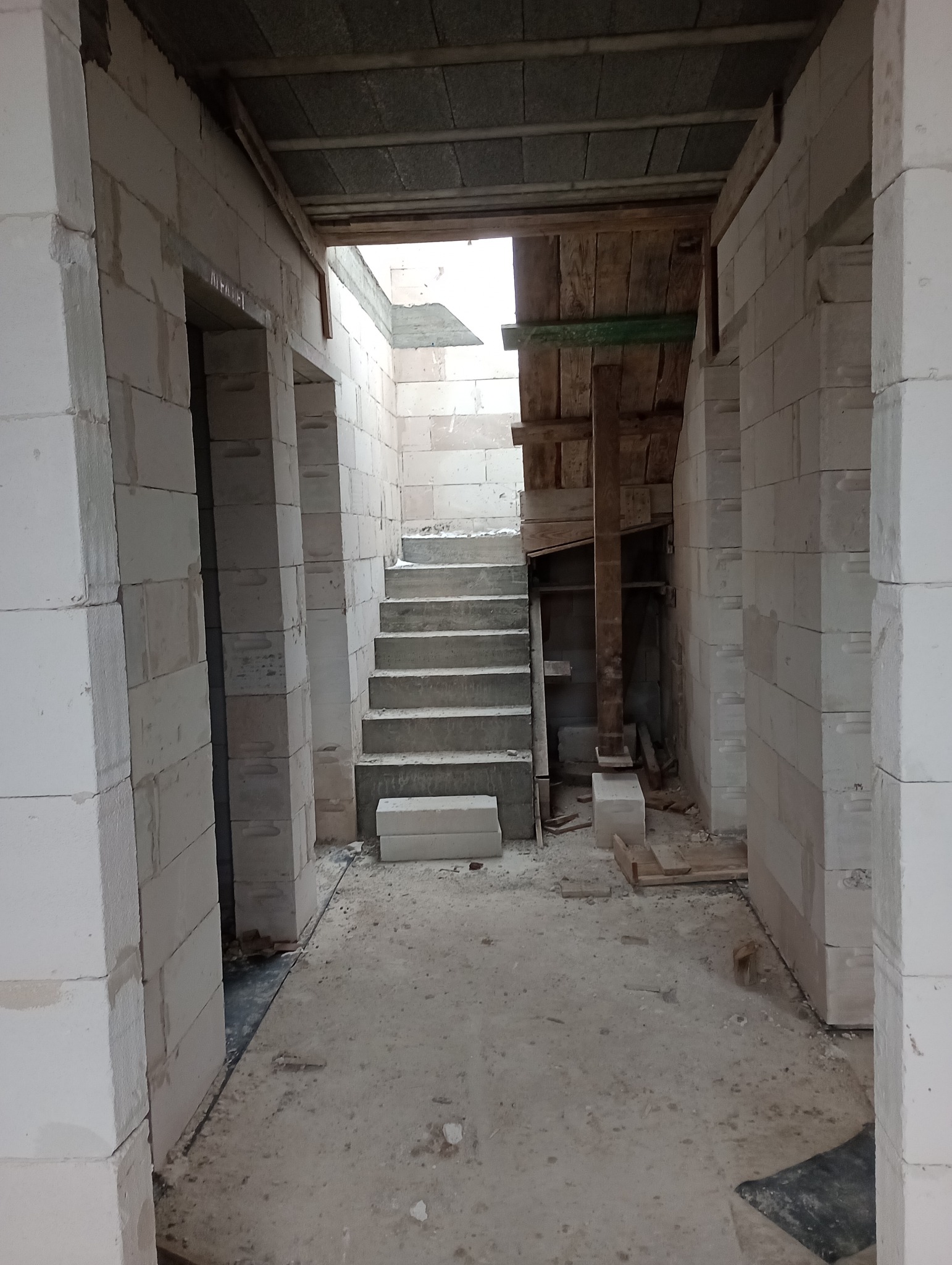 Wnętrze budynku w trakcie budowy schodów, widoczne białe bloczki konstrukcyjne i drewniane szalunki.