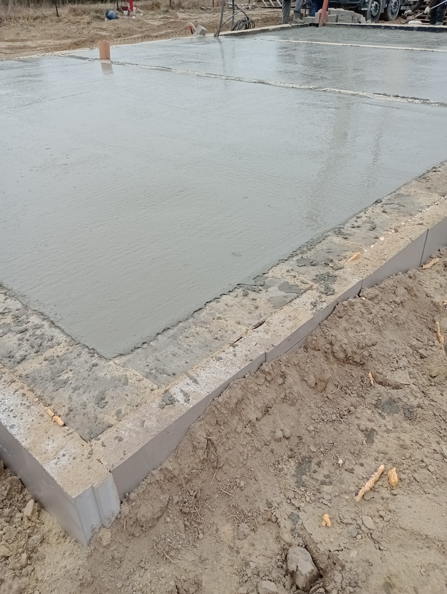 Wylany fundament betonowy w Lublinie, widoczne szalunki i świeży beton. W tle ekipa budowlana i betoniarka.