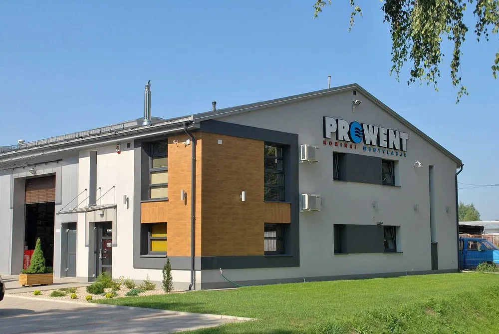 Nowoczesny budynek magazynowo-biurowy z logo firmy PROWENT, widoczne klimatyzatory na elewacji, zadbany trawnik przed budynkiem.