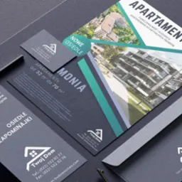 Zestaw materiałów firmowych, w tym wizytówka, ulotka reklamowa z wizualizacją osiedla apartamentów, koperta i ołówek, ułożone na ciemnoszarym tle.