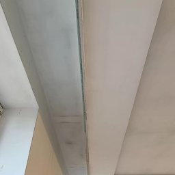 Aleksandra Szymborska CREO COMPANY - Fragment sufitu z widocznymi elementami konstrukcyjnymi przed wykończeniem, szpachlowany fragment sufitu przy ścianie, widoczne łączenia płyt gipsowo-kartonowych.