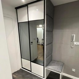 Aleksandra Szymborska CREO COMPANY - Nowoczesna szafa wnękowa z przesuwnymi drzwiami lustrzanymi, połączona z tapicerowanym siedziskiem i panelem ściennym w odcieniach szarości, tworząca funkcjonalną strefę wejściową w mieszkaniu.