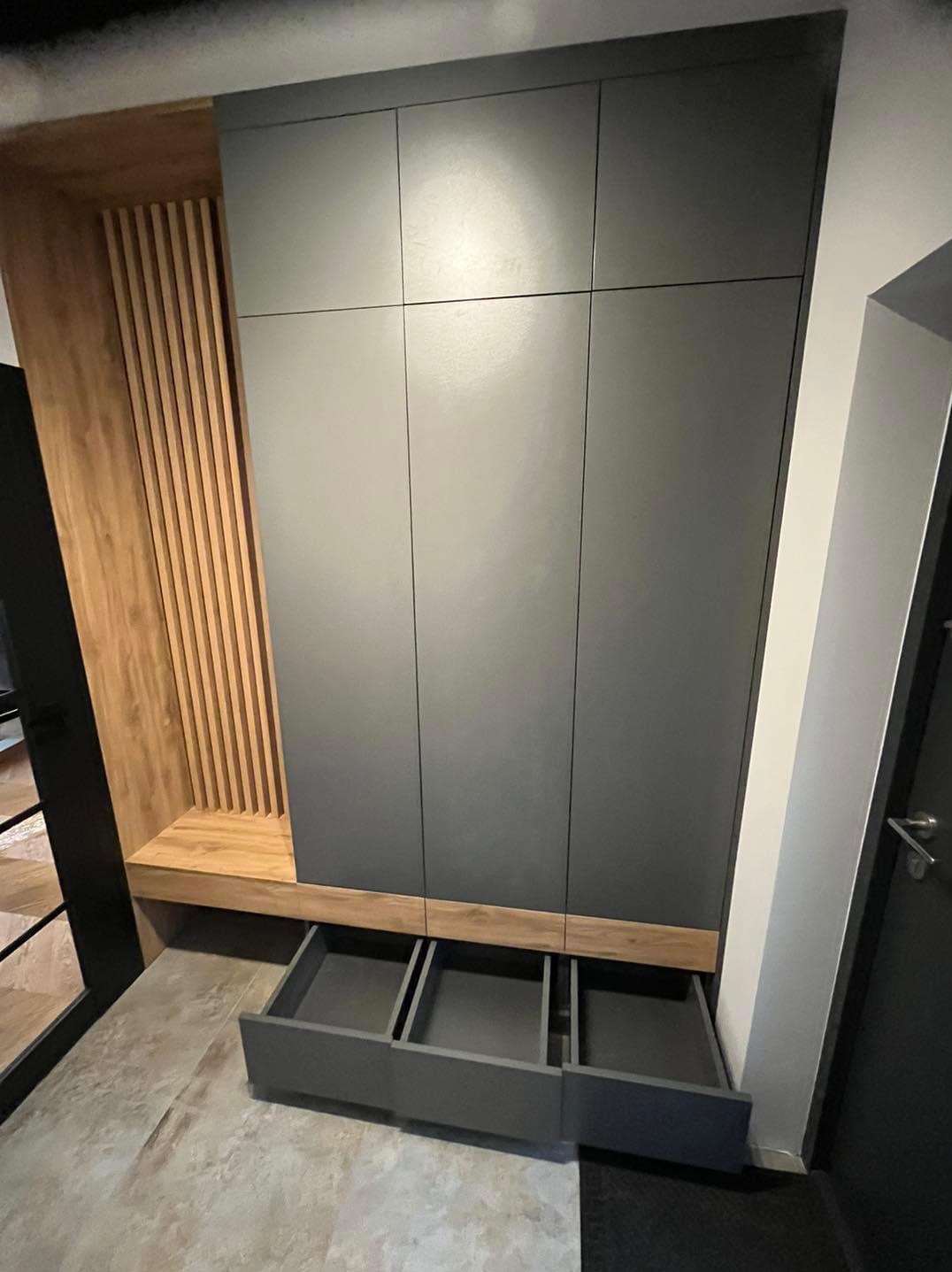 Nowoczesna zabudowa wnęki z szarymi frontami szafek i drewnianymi akcentami, otwarte szuflady eksponują minimalistyczny design.