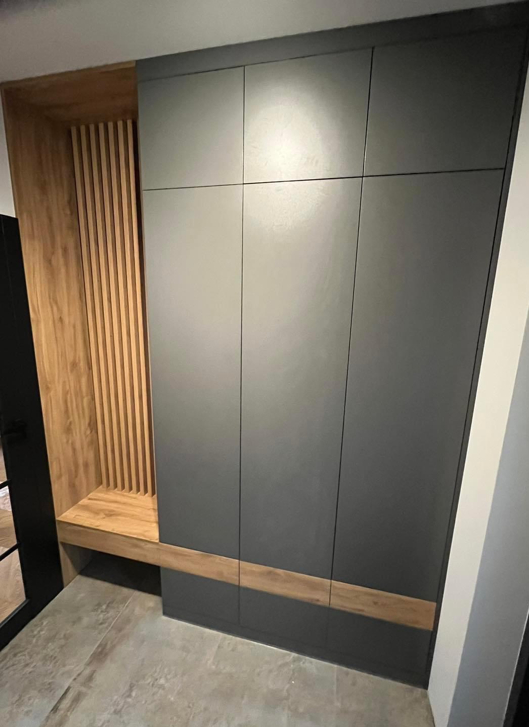 Nowoczesna zabudowa przedpokoju z szarą szafą wnękową i drewnianym siedziskiem z ażurową ścianką z pionowych listew.