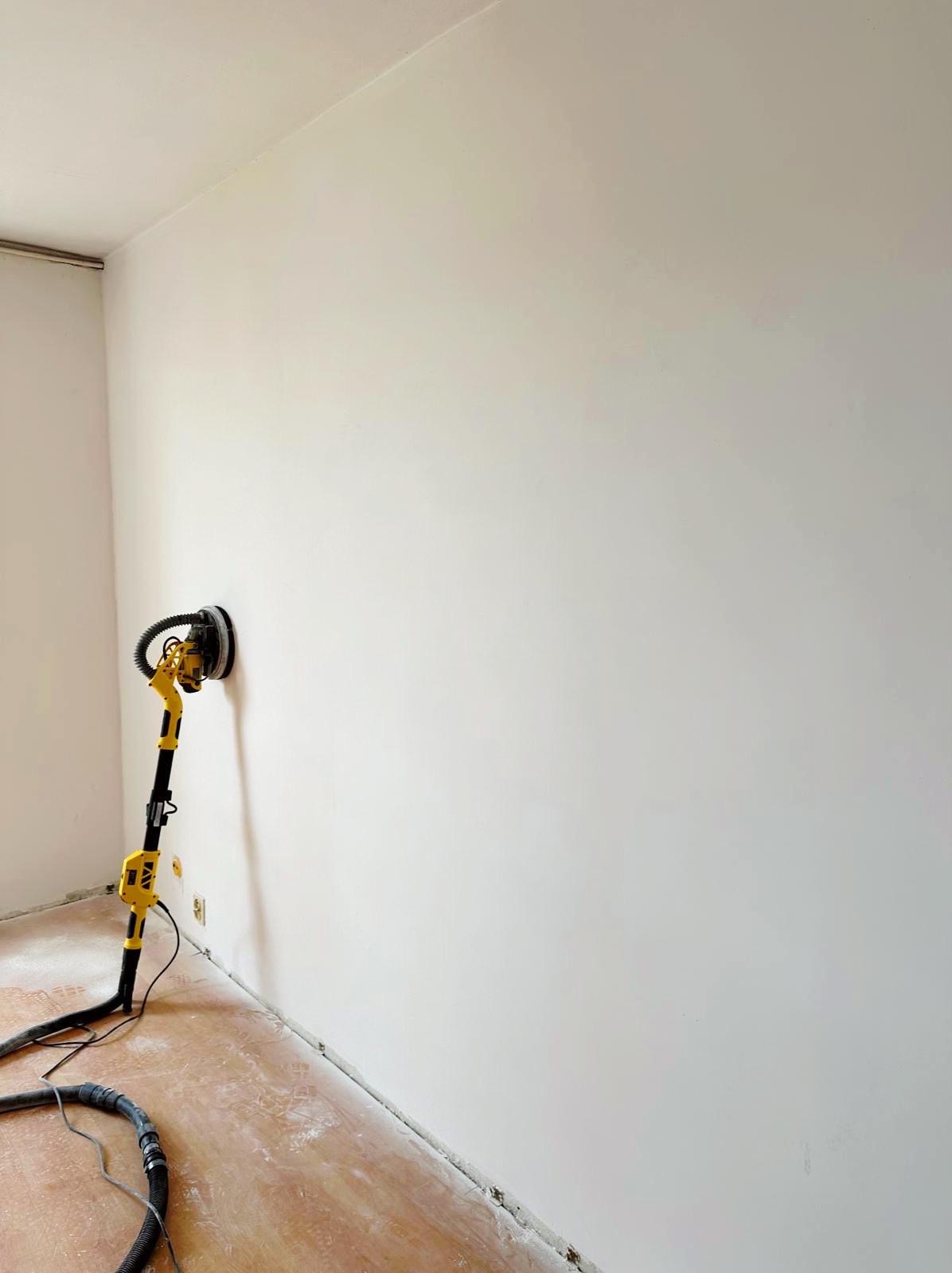 Ściana po szpachlowaniu, przygotowana do malowania, szlifierka do gładzi na podłodze, widoczne ślady po szpachlowaniu i szlifowaniu.