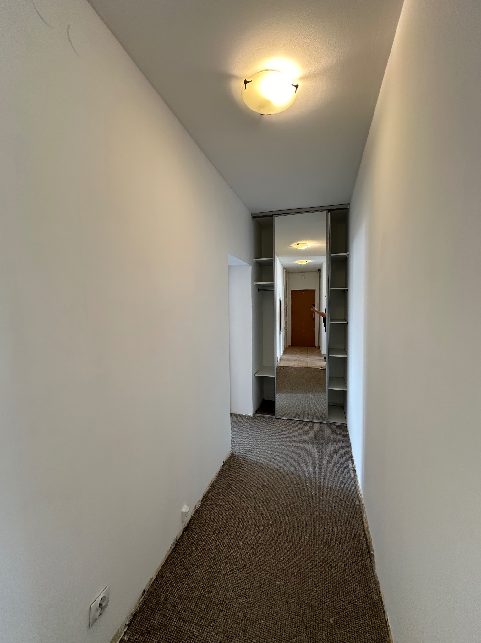 Korytarz w mieszkaniu po odświeżeniu ścian, widoczne ślady po niedokładnym zabezpieczeniu podłogi dywanowej przy listwach przypodłogowych i gładkie, białe powierzchnie ścian.