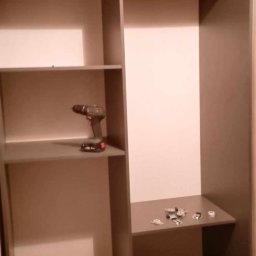 Olszówka - Wnętrze szafy wnękowej w trakcie montażu, z widoczną wkrętarką akumulatorową na półce i elementami mocującymi na dolnej półce.
