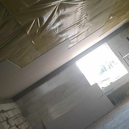 Olszówka - Wnętrze w trakcie prac, widoczne ocieplenie poddasza folią, zamontowane płyty gipsowo-kartonowe, surowa ściana z bloczków i okno w tle.