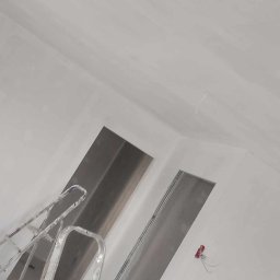 Olszówka - Wnętrze w trakcie prac wykończeniowych, widoczna aluminiowa drabina oparta o ścianę, sufit i ściany świeżo pomalowane na biało, widoczne kable elektryczne wystające ze ściany.