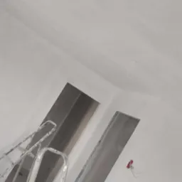 Wnętrze w trakcie prac wykończeniowych, widoczna aluminiowa drabina oparta o ścianę, sufit i ściany świeżo pomalowane na biało, widoczne kable elektryczne wystające ze ściany.