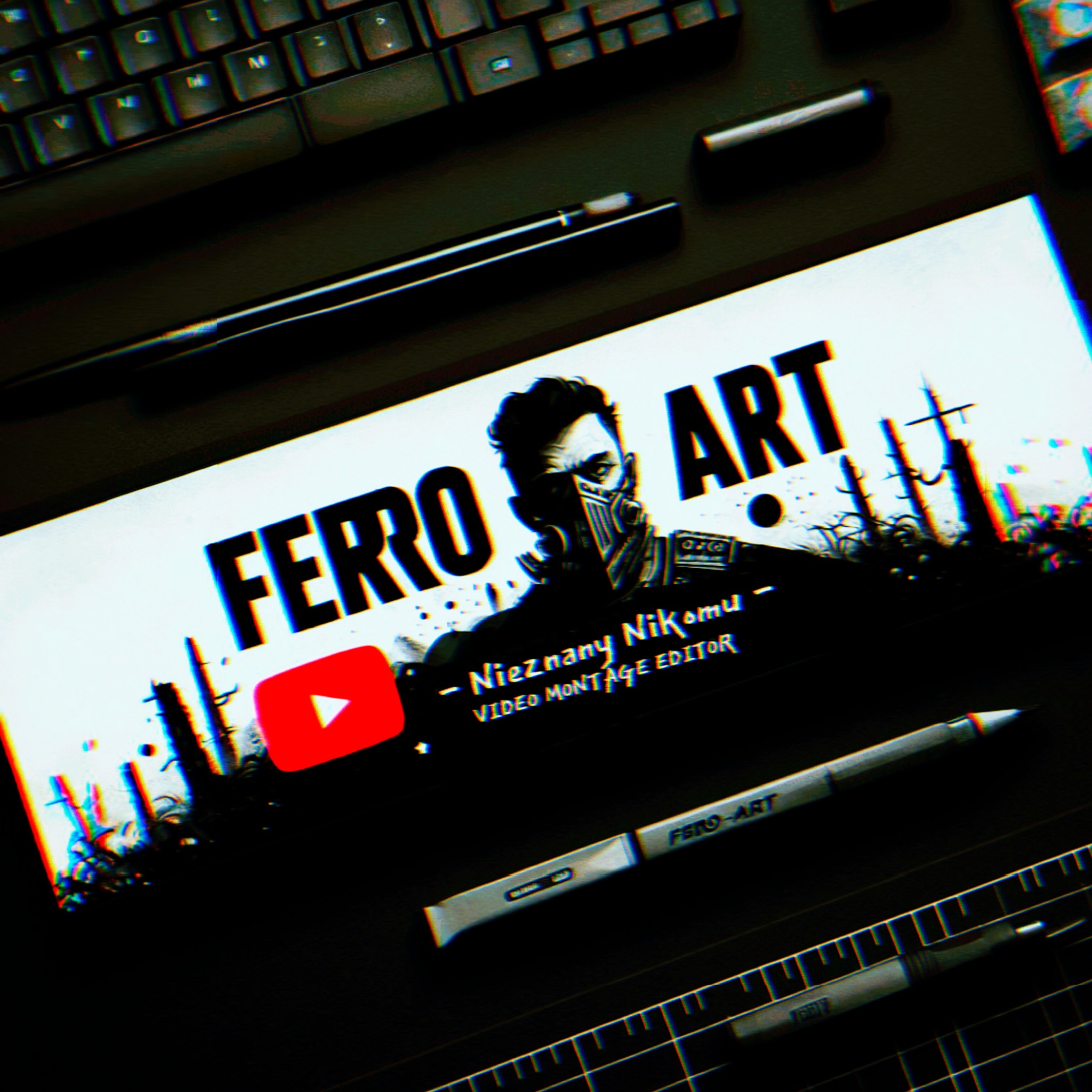 Ekran z grafiką 'FERO ART', logo YouTube, podpisem 'Video Montage Editor', otoczony klawiaturą, długopisami i linijką kreślarską. Ujęcie z góry, ciemne tło.