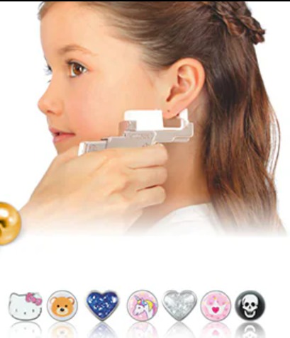 Dziewczynka podczas bezhukowego przekłuwania ucha aparatem STUDEX®, widoczne kolczyki ze stali chirurgicznej z różnymi wzorami na dole kadru.